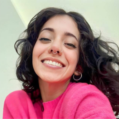 Smiling woman in a pink sweater with curly hair and a nose ring, promoting หลุด OnlyFans content with a cheerful expression.